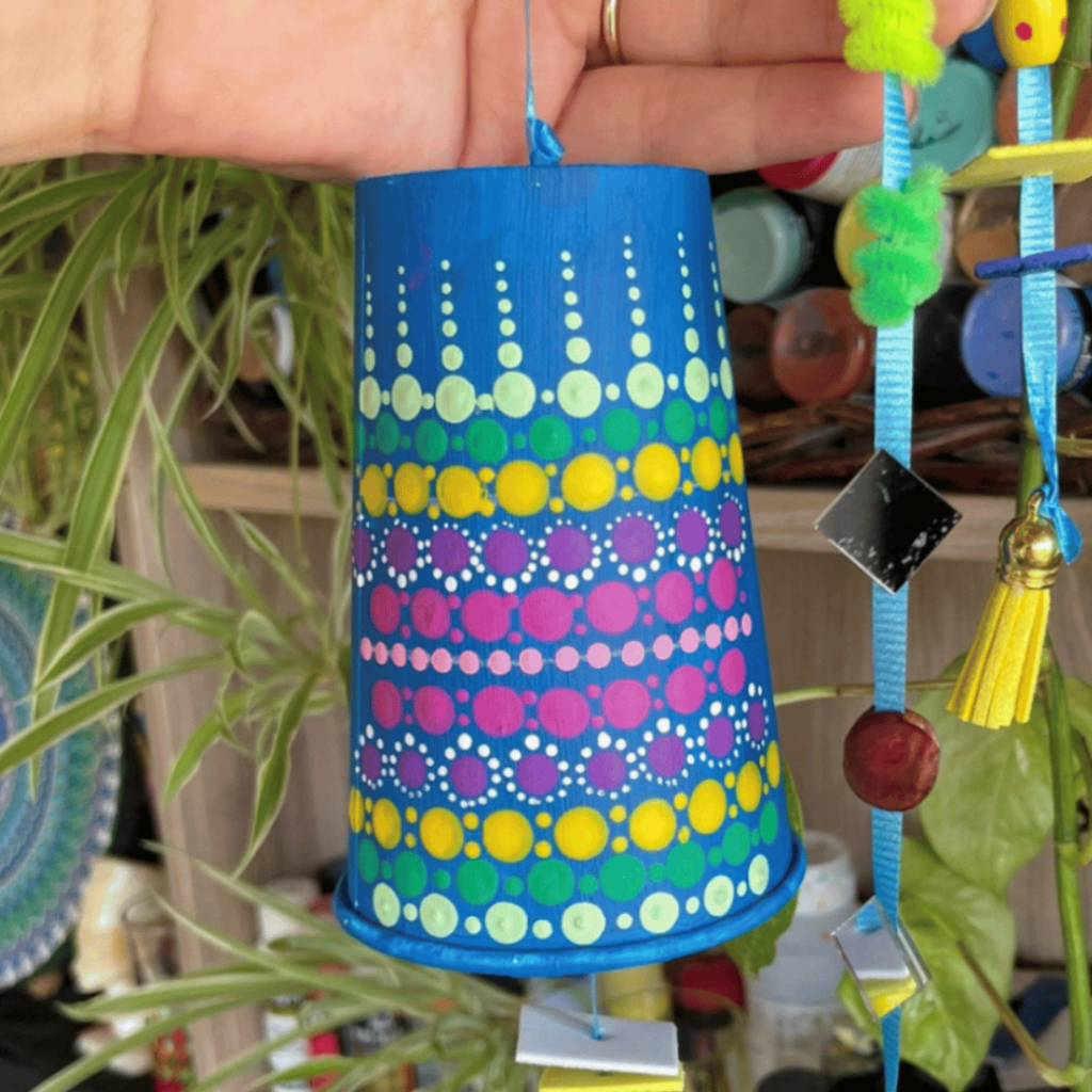 פעמון כחול עם נקודות צבעוניות תלוי בין צמחים